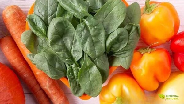 Frutas, legumes e verduras coloridos ricos em carotenoides dispostos lado a lado sobre superfície clara
