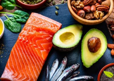 Variedade de alimentos contendo gorduras saturadas e insaturadas dispostos sobre mesa de madeira: salmão fresco, abacate, castanhas, nozes e azeite de oliva. As gorduras insaturadas (ômega 3, 6 e 9) presentes nestes alimentos ajudam a reduzir colesterol LDL, proteger o coração e melhorar função cerebral. Consumir esta diversidade garante perfil lipídico completo para saúde ótima.