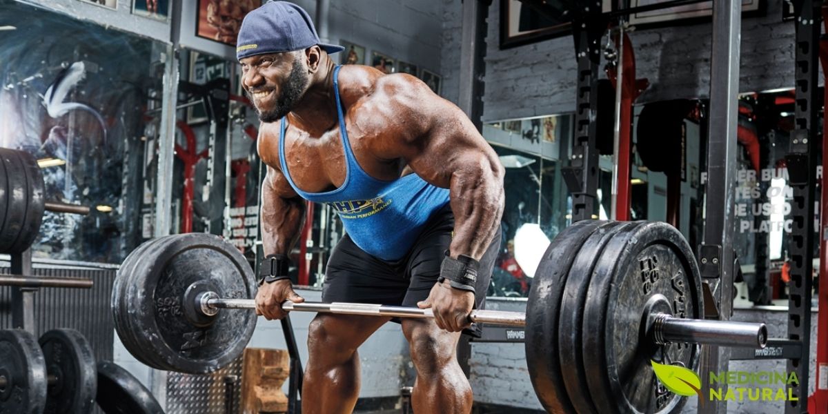 Atleta masculino executando agachamento livre com barra pesada em academia profissional, demonstrando a técnica correta para um dos exercícios mais eficazes para hipertrofia de membros inferiores. O agachamento é um movimento composto que ativa múltiplos grupos musculares simultaneamente, gerando um potente estímulo mecânico que ativa a via mTORC1 e promove o crescimento muscular. A combinação de treino de força progressivo com nutrição adequada é a chave para maximizar os ganhos de massa muscular. Fonte: Muscle & Strength.
