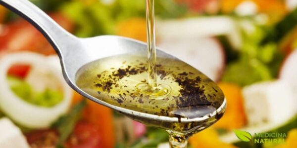 Azeite de oliva extra virgem sendo despejado de garrafa de vidro sobre salada fresca em tigela branca, com folhas verdes, tomates e outros vegetais coloridos ao fundo. Imagem que ilustra o uso prático do azeite como tempero saudável, rico em ácido oleico (ômega 9) e polifenóis antioxidantes. O azeite de oliva extra virgem é considerado o padrão-ouro entre os óleos vegetais, com benefícios cardiovasculares comprovados pelo estudo PREDIMED (30% de redução em eventos cardiovasculares).