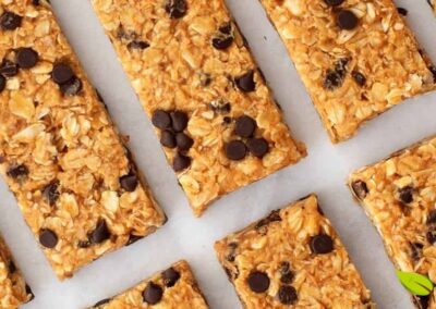 Barras de granola caseiras cortadas em porções uniformes e perfeitamente alinhadas sobre papel manteiga branco, demonstrando a técnica adequada de preparação e apresentação. A imagem exemplifica o resultado final de uma receita bem executada de barras de proteína pelo método a frio, onde a textura firme mas não dura permite cortes limpos e precisos.