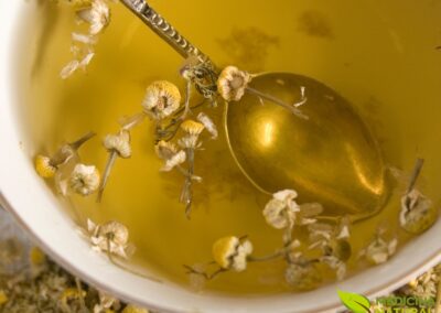 Uma xícara com chá de camomila quente, decorada com flores frescas ao lado. A cor dourada do chá e o vapor subindo criam uma atmosfera acolhedora e relaxante.