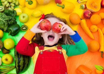 Uma criança radiante posando com uma abundância de frutas e vegetais frescos demonstra o entusiasmo que pode ser cultivado em torno de alimentos saudáveis. Envolver as crianças na escolha, compra e preparação de alimentos coloridos pode transformar a resistência em curiosidade e aceitação.