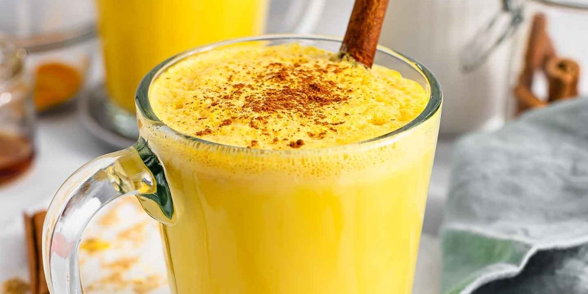 Golden Milk decorado com canela em pó, acompanhado de especiarias aromáticas. Esta versão enriquecida do chá de cúrcuma combina múltiplas especiarias como gengibre, cardamomo e noz-moscada, potencializando os efeitos anti-inflamatórios e antioxidantes. Excelente para consumo noturno, promovendo relaxamento e sono reparador.