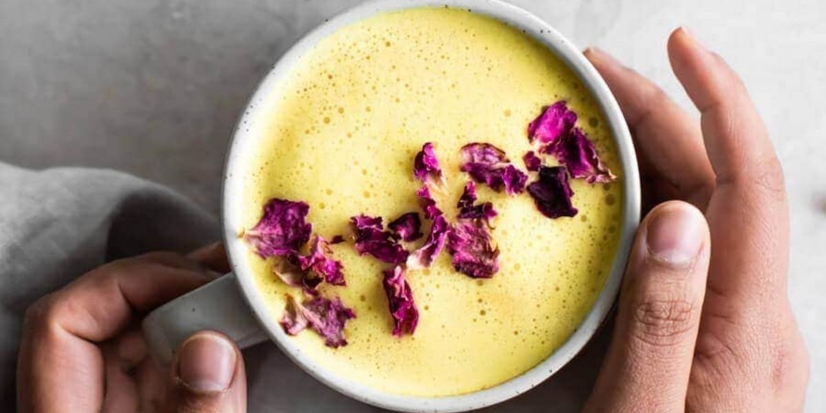 Golden Milk latte cremoso, decorado artisticamente com especiarias. Esta versão sofisticada do chá de cúrcuma utiliza leite vaporizado para criar textura aveludada, combinando benefícios terapêuticos com experiência sensorial premium. Popular em cafeterias especializadas em bebidas funcionais.