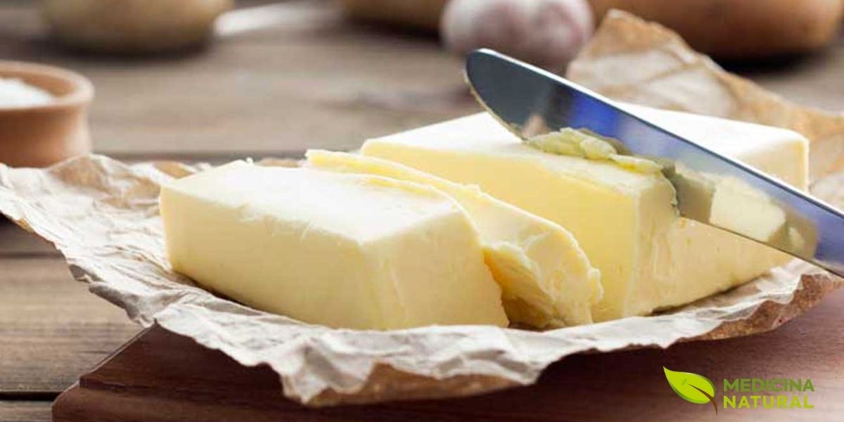 Tablete de manteiga natural sobre tábua de madeira com faca. A manteiga é fonte de gordura saturada, contendo ácido butírico que tem propriedades anti-inflamatórias para o intestino. Embora seja gordura saturada, é um alimento natural, preferível à margarina ultraprocessada. Deve ser consumida com moderação (1-2 colheres de chá/dia).