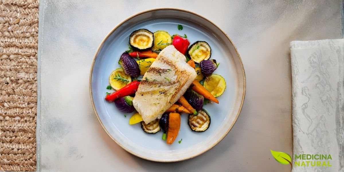 Refeição equilibrada com peixe grelhado e vegetais assados coloridos. Este tipo de preparação é ideal para férias na praia ou em restaurantes, oferecendo proteína de qualidade, gorduras saudáveis e uma variedade de nutrientes essenciais sem excesso de calorias.