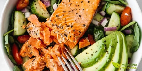 Salada vibrante e nutritiva combinando folhas verdes frescas, tomates-cereja, salmão grelhado em cubos, fatias de abacate maduro, pepino e molho leve. Prato completo que exemplifica refeição rica em gorduras boas: ômega 3 do salmão (EPA e DHA), ômega 9 do abacate, fibras e antioxidantes dos vegetais. Ideal para saúde cardiovascular, saciedade prolongada e controle glicêmico, demonstrando como gorduras saudáveis tornam refeições mais saborosas e nutritivas.