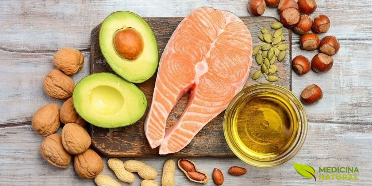 Trio poderoso de gorduras boas: filé de salmão fresco, abacate maduro cortado e nozes inteiras dispostos sobre superfície de madeira rústica clara. Estes três alimentos combinam ômega 3 (EPA e DHA do salmão), ômega 9 (ácido oleico do abacate) e ômega 3 vegetal (ALA das nozes), formando um perfil lipídico completo para proteção cardiovascular.