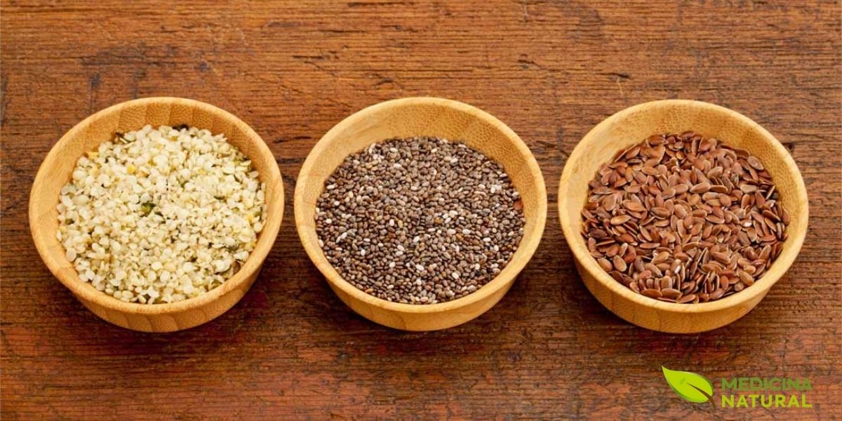 Sementes de chia pretas, sementes de linhaça dourada e sementes de cânhamo descascadas - formando uma composição visualmente harmoniosa. Esta imagem celebra os ingredientes funcionais que elevam o perfil nutricional das barras de proteína caseiras a um nível superior, destacando três das fontes vegetais mais ricas em ácidos graxos ômega-3, proteínas completas e fibras solúveis. As sementes de chia, pequenas e escuras, são conhecidas por sua capacidade de absorver até 12 vezes seu peso em água, criando um gel que atua como ligante natural. A linhaça dourada oferece lignanas com propriedades antioxidantes, enquanto as sementes de cânhamo fornecem todos os nove aminoácidos essenciais. Juntas, estas sementes transformam uma simples barra em um superalimento portátil.