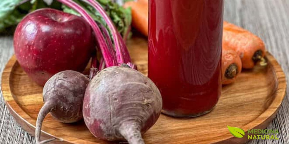 Suco energético de beterraba e cenoura, ideal para consumo pré-treino devido ao seu alto teor de nitratos que aumentam a produção de óxido nítrico. Os vegetais frescos ao fundo reforçam a origem natural dos nutrientes, mostrando que a energia sustentável vem de fontes alimentares reais.